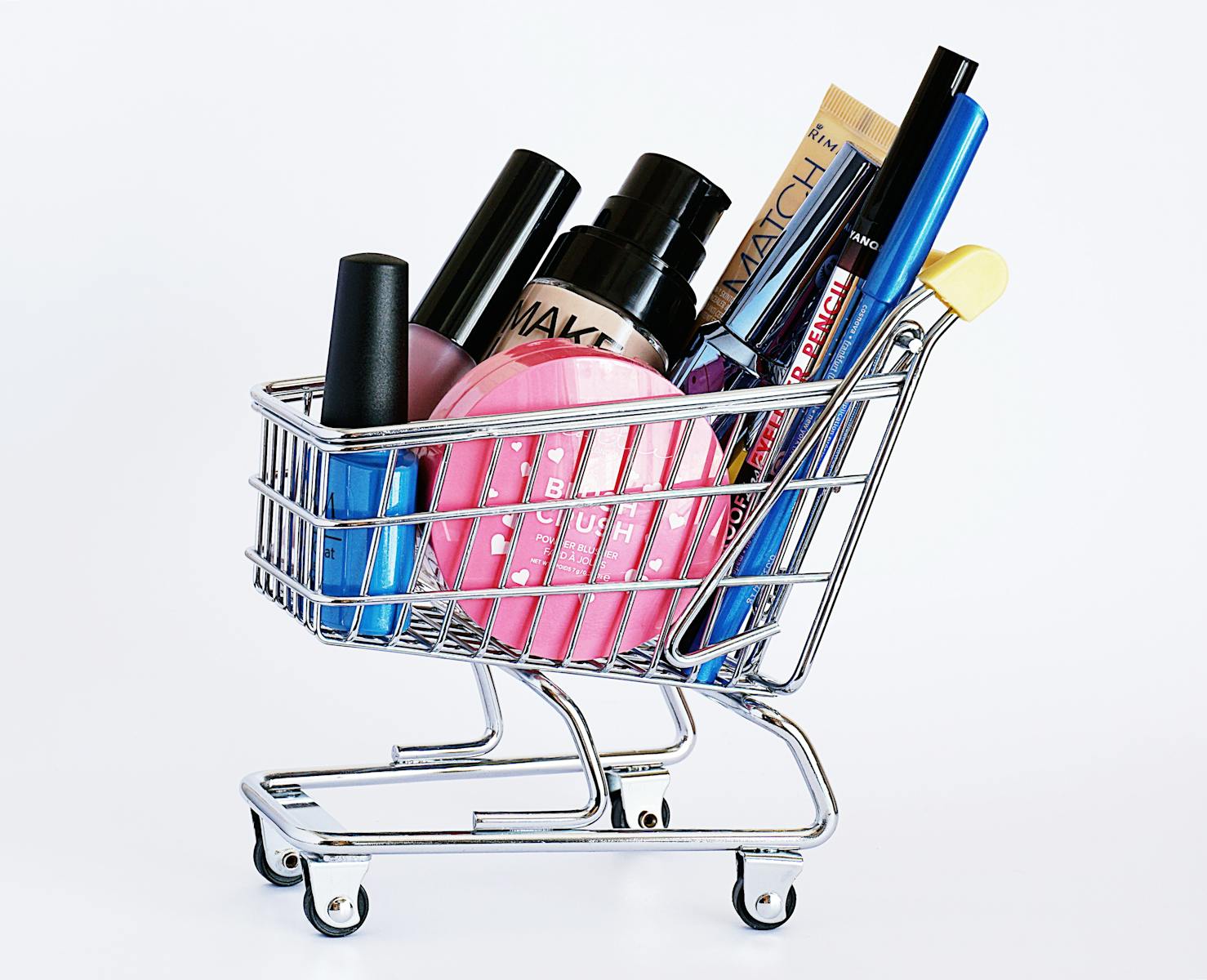 Miniature shopping cart filled with a variety of cosmetics on a white background. merchandiser